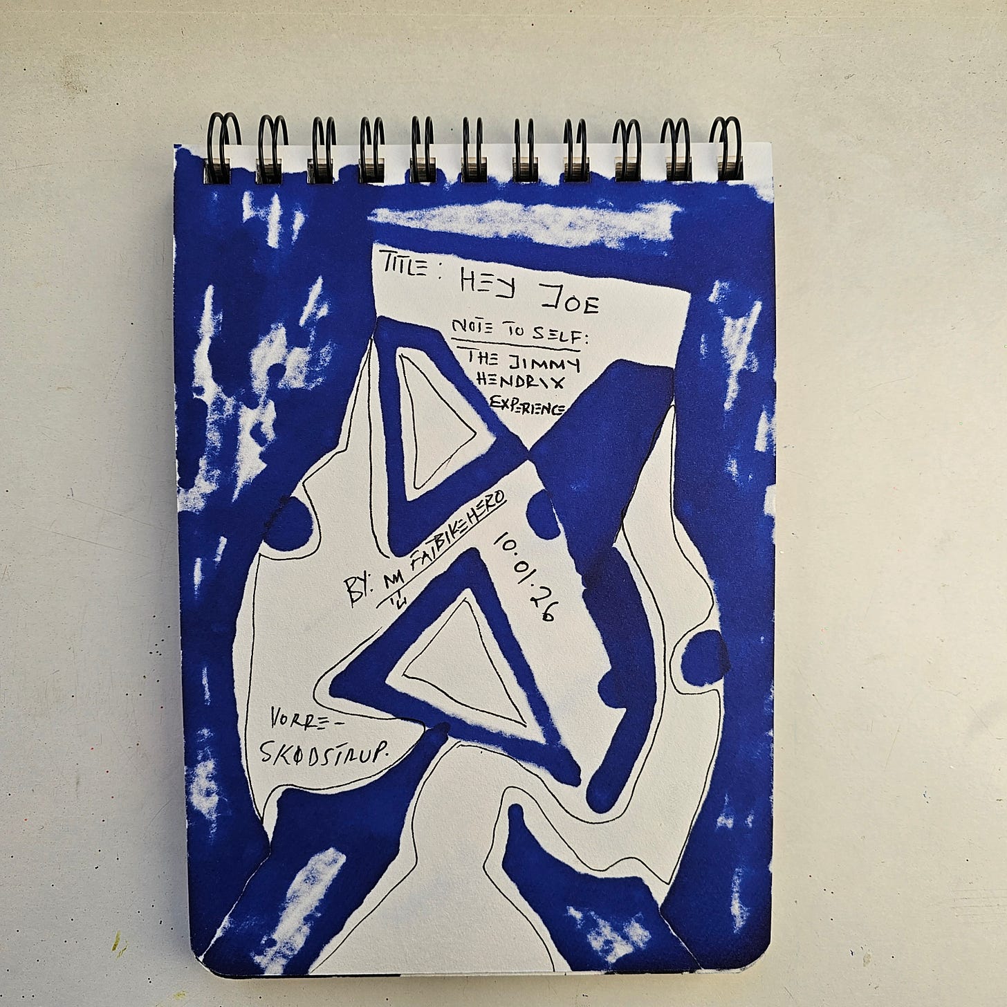 Alt Text:     The reverse side of a sketchbook page by artist FatbikeHero, heavily covered in deep blue marker. Handwritten text in the center reads "TITLE: HEY JOE," "NOTE TO SELF: THE JIMMY HENDRIX EXPERIENCE," and "BY: M FATBIKEHERO." The date "10.01.26" and location "VORRE - SKØDSTRUP" are inscribed in black ink within the white negative space.