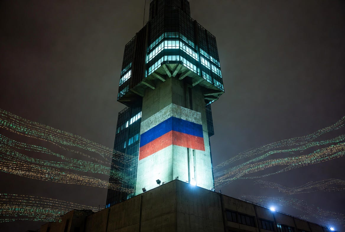 Cinematic night shot of a brutalist Russian skyscraper with a Russian tricolor flag lit by floodlights on the facade, streams of glowing digital transaction data flowing in the foreground, representing the Kremlin-backed A7A5 shadow financial network. Cinematic night shot of a brutalist Russian skyscraper with a Russian tricolor flag lit by floodlights on the facade, streams of glowing digital transaction data flowing in the foreground, representing the Kremlin-backed A7A5 shadow financial network.