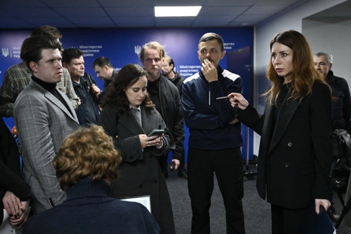 Svitlana Grynchuk, standing at right, speaks with journalists in a room with a blue Ministry of Energy backdrop.