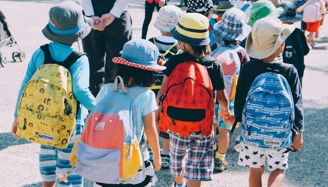group of people wearing white and orange backpacks walking on gray concrete pavement during daytime