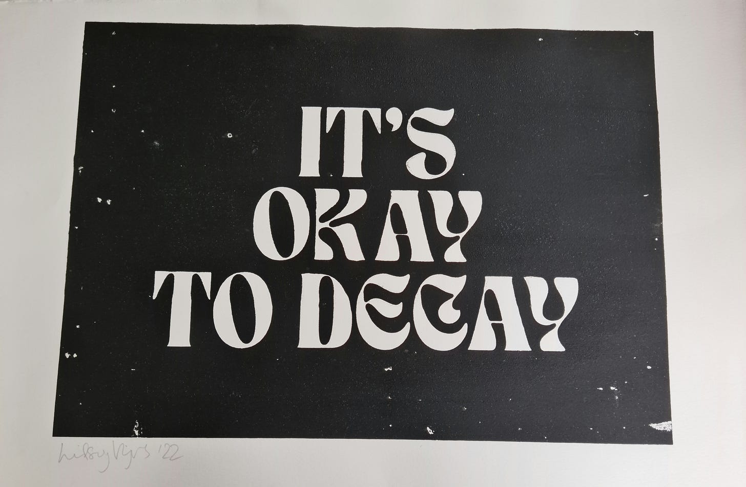 A hand-pulled screen print by LV. White text that says IT'S OKAY TO DECAY on a black ink background. A hand-pulled screen print by LV. White text that says IT'S OKAY TO DECAY on a black ink background.