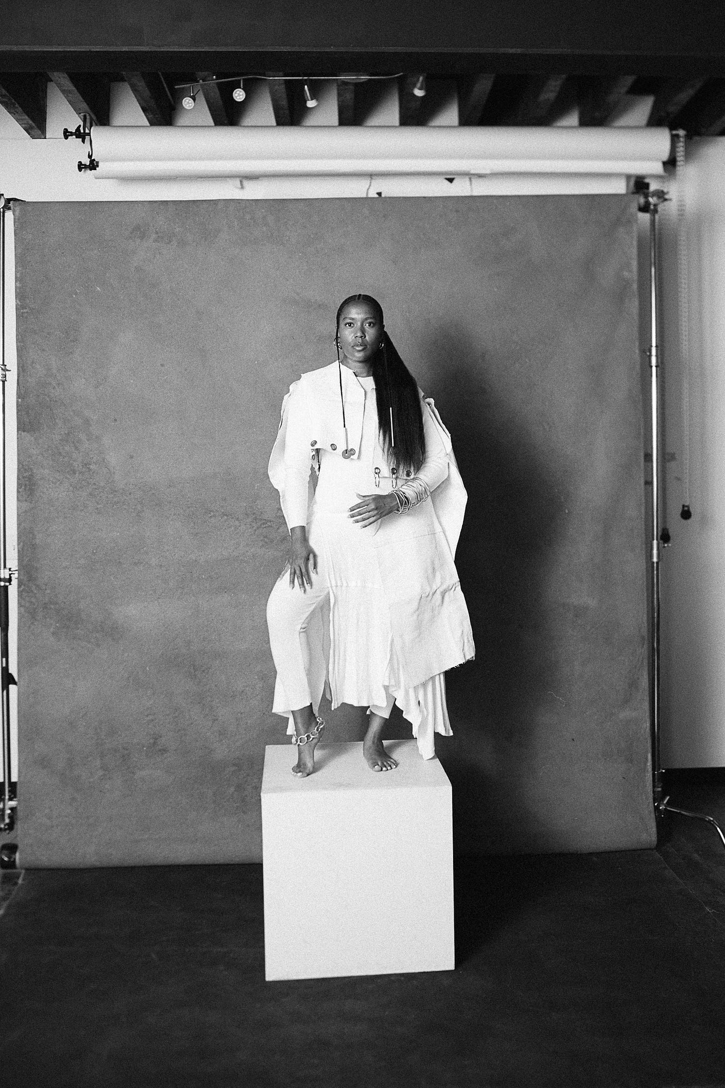 Black and white photograph of me looking directly into the camera, posing on a white pedastal while wearing AYZACO workwear. Photographer: Stephen L.A. Miller Black and white photograph of me looking directly into the camera, posing on a white pedastal while wearing AYZACO workwear. Photographer: Stephen L.A. Miller