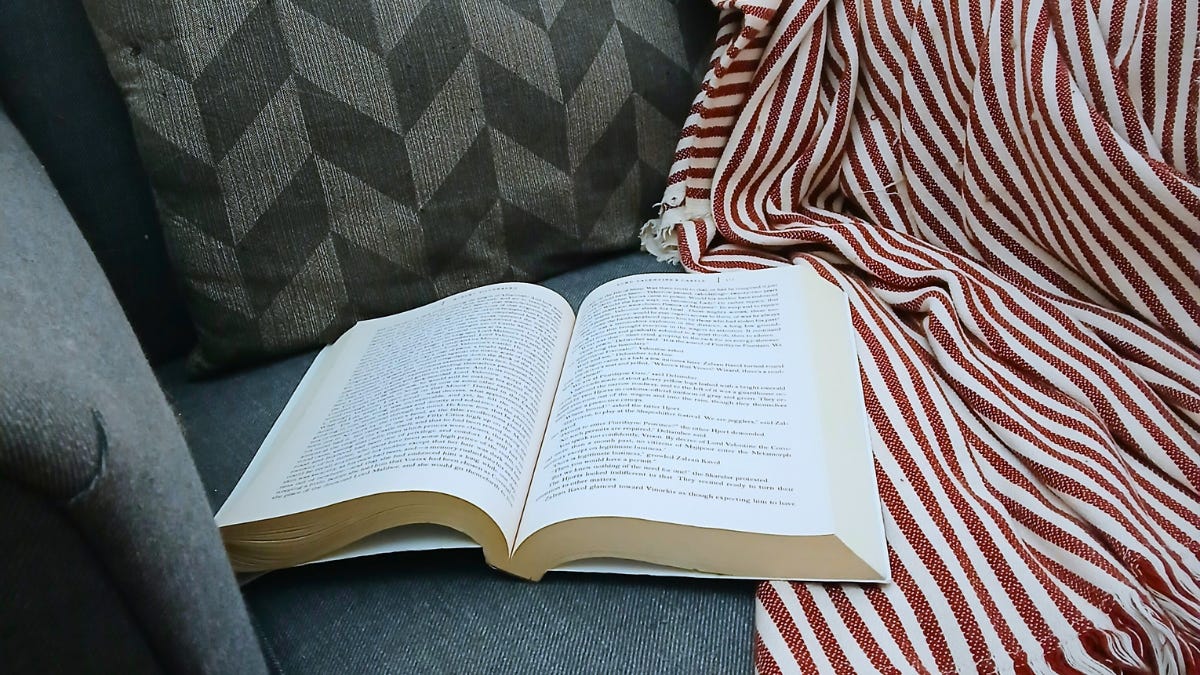 Close-up of open book on grey chair and cream-and-red striped blanket Close-up of open book on grey chair and cream-and-red striped blanket