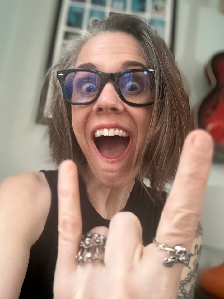 two women each with wide open mouths smiling while throwing the "goat" with their hands and fingers.