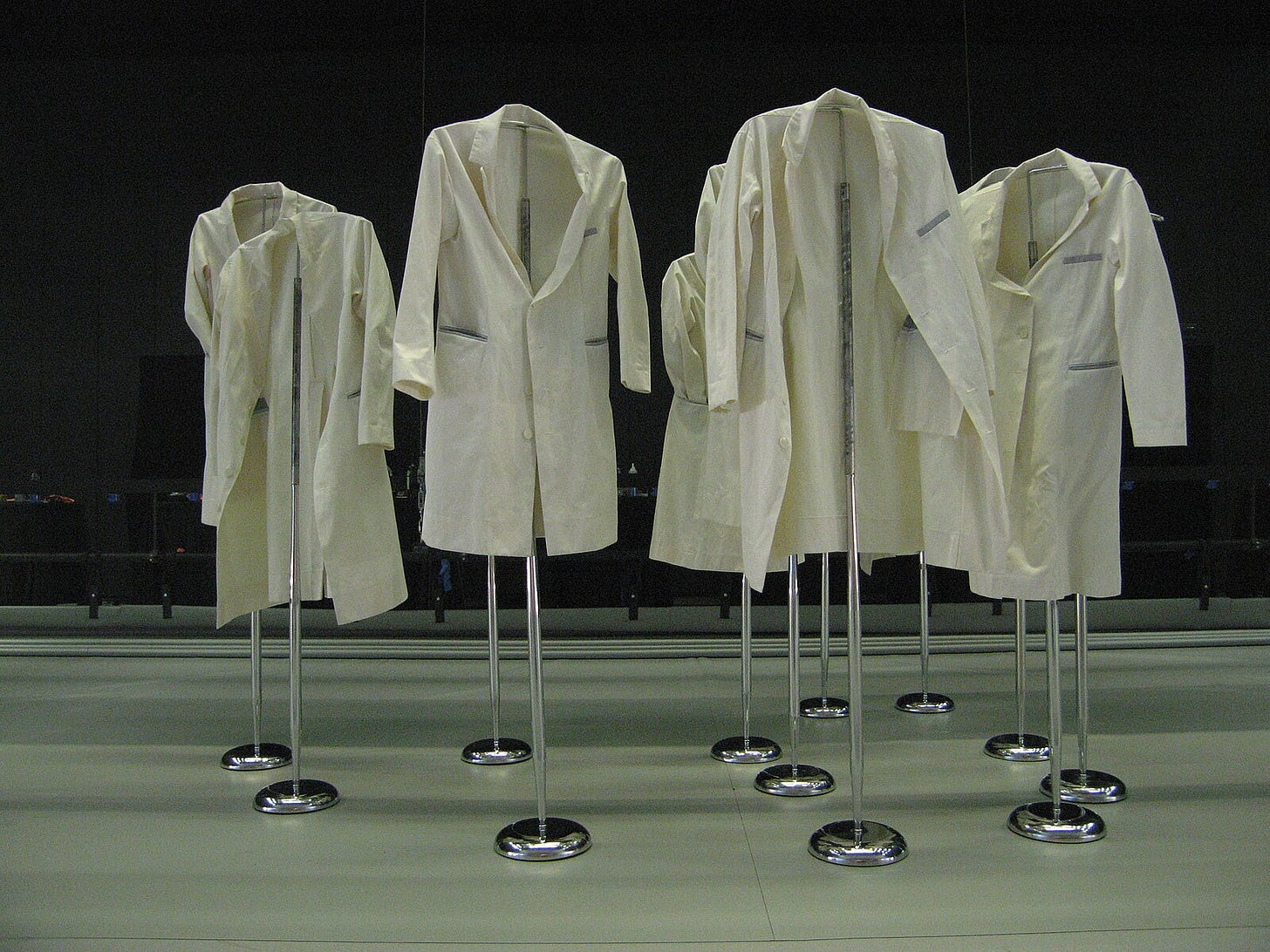 “Photographic and archival imagery of individuals wearing white lab coats as used in the design studio of Maison Martin Margiela. These garments functioned as a symbolic uniform to neutralize hierarchy, promote anonymity, and emphasize collective authorship over individual style. The white coats reflect the psychological and symbolic aspects of enclothed cognition — clothing as a trigger for behavior, identity, and group dynamics.”
