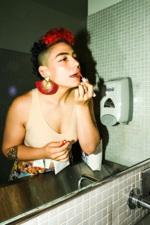 A woman is applying makeup while looking in a mirror.