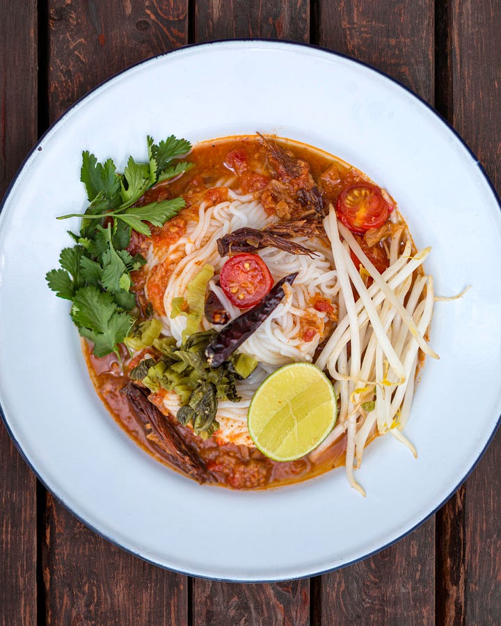 bowl of soupy red curry with chunks of small tomatoes, fresh coriander, and bean sprouts