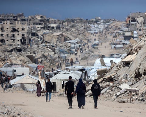 People walk among the rubble of buildings destroyed by Israeli airstrikes.