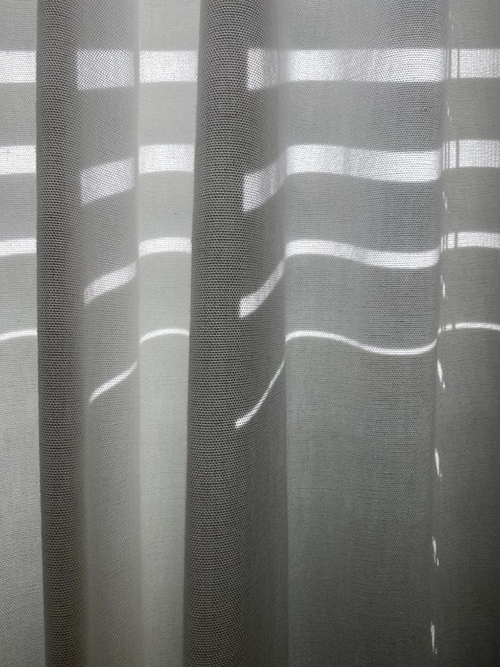 A close-up of light shining through Venetian blinds onto curtains, making wavy lines of light
