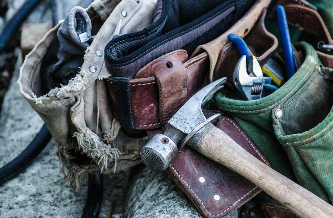 collection of well-used tools including brown handled hammer and tool belt