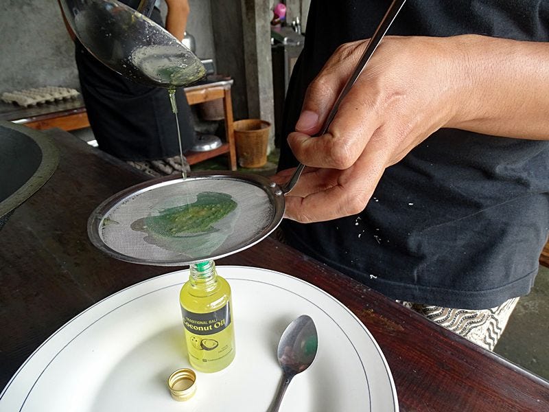 Fresh coconut oil being filtered through a fine mesh into a small glass bottle in a traditional Balinese kitchen.