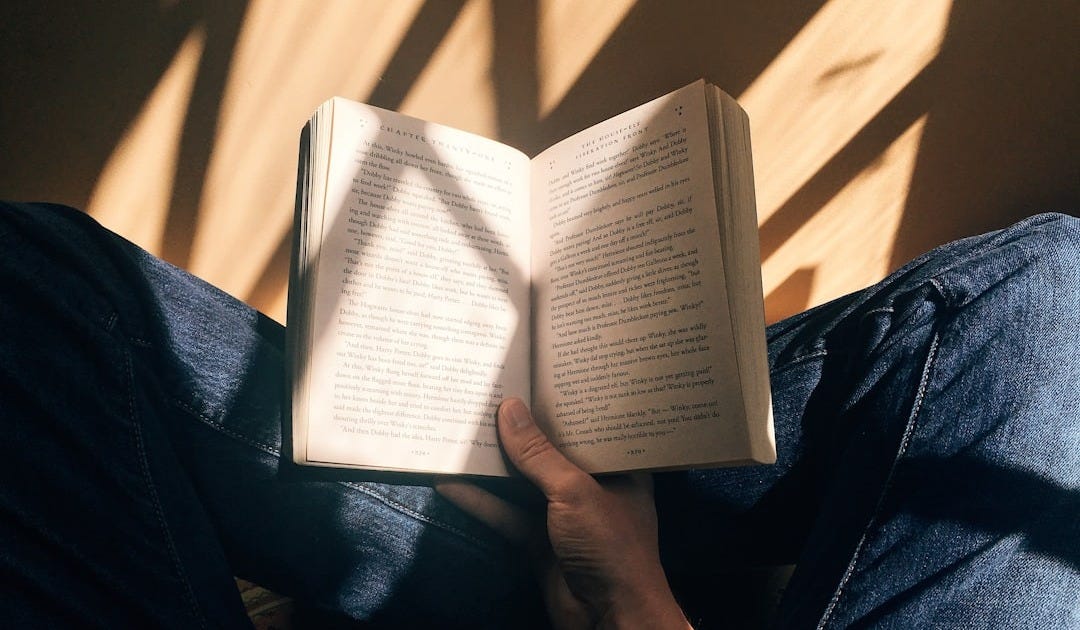 person holding book sitting on brown surface