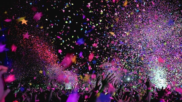 Photo of crowd with hands raised and colourful confetti above them. Photo of crowd with hands raised and colourful confetti above them.