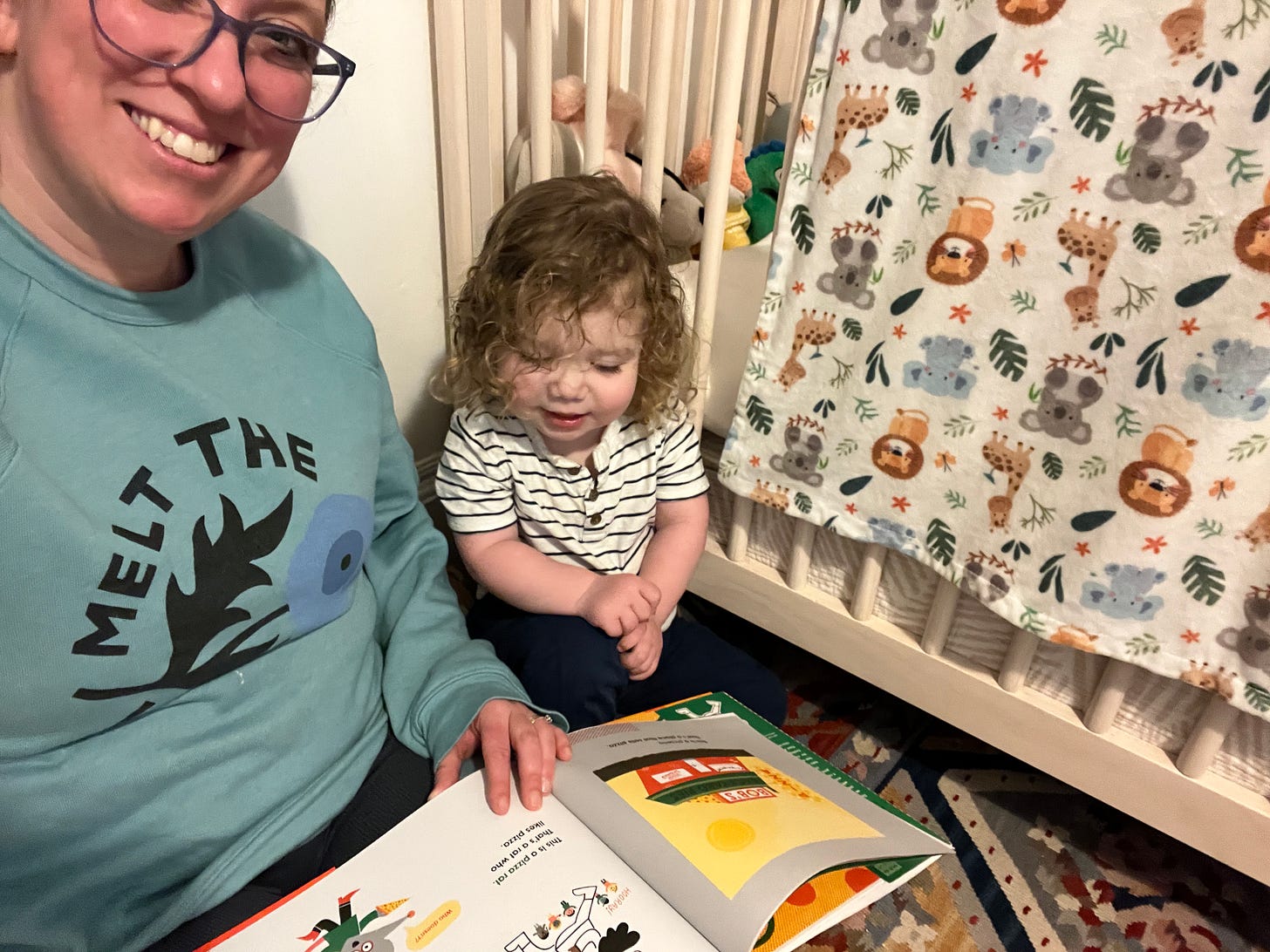 A woman and a toddler read a picture book about the history of pizza.