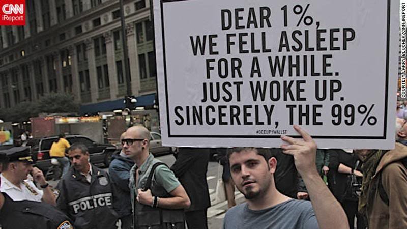 Occupy Wall Street protester holding a sign that says Dear 1%, we fell asleep for a while. Just work up. Sincerely, the 99%