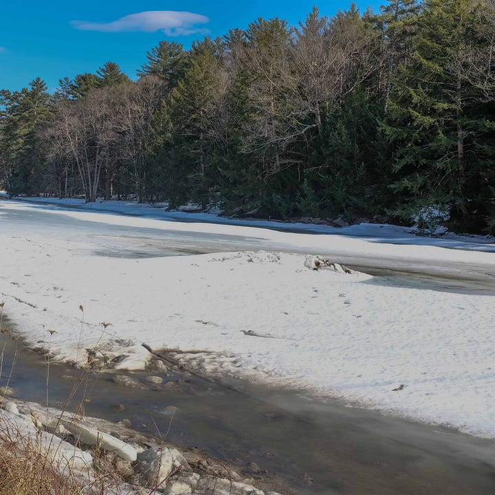 Four photographs of a snow covered rock in the middle of an icy river, which is melting so there is water flowing in the third and forth images.