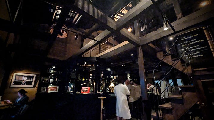 Two cocktails on a table. A nighttime bar scene with thick wooden ceiling beams and dim lighting.