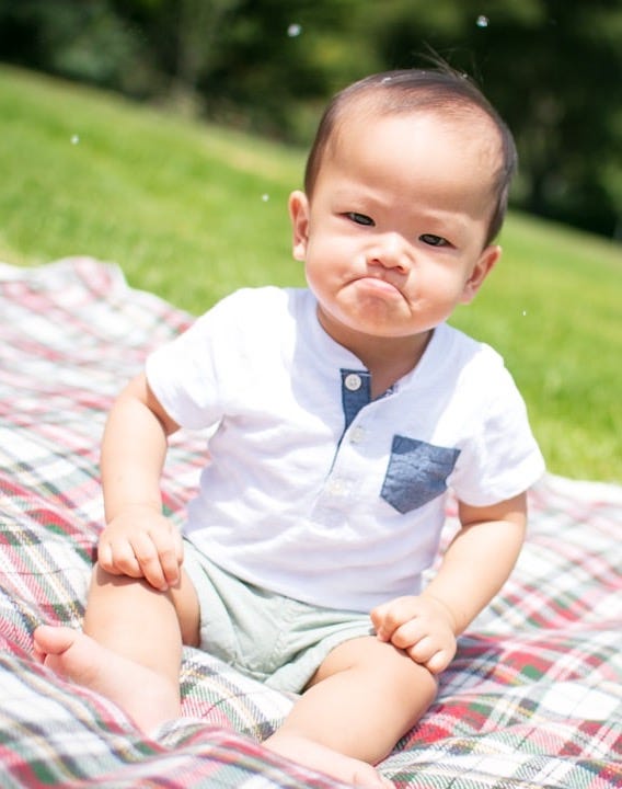 selective focus photography of grumpy face toddler sitting on plaid pad taken during daytime
