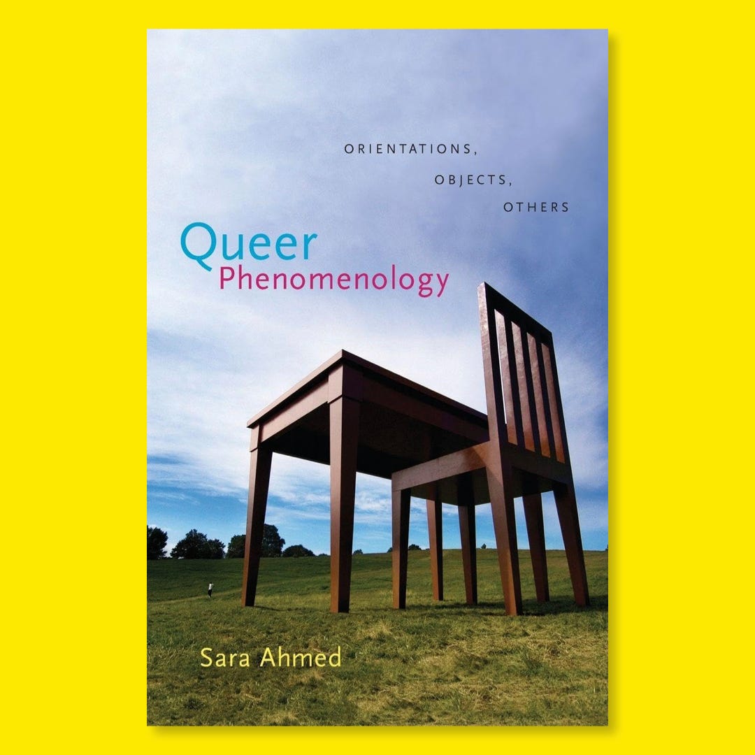 The cover of the book by Sara Ahmed shows a green hill with some trees at its edge against a blue sky with light clouds. On the hill stands an oversized wooden desk with a matching desk chair facing the treeline. A tiny person is standing to the left of the table. They're not really visible except that they're wearing a white shirt and dark trousers.
