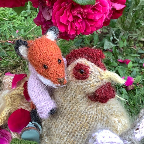 Knitted toys under a red rose bush surrounded by fallen petals
