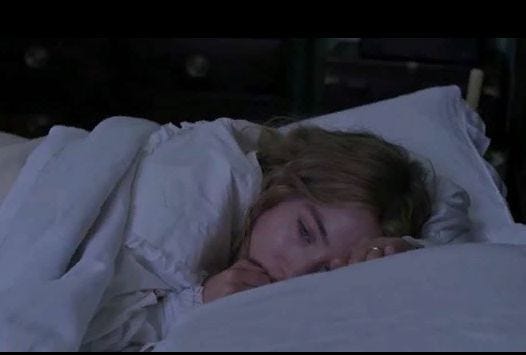 This may contain: a woman is laying in bed with her head on the pillow and looking at the camera