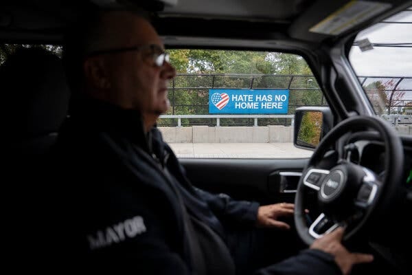 Mr. Gonnelli behind the steering wheel of his car. Outside the driver’s side window is a sign that says “Hate Has No Home Here.”