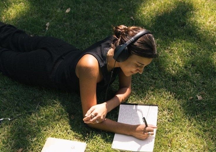 This may contain: a woman laying on the grass writing in her notebook This may contain: a woman laying on the grass writing in her notebook