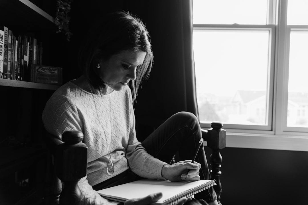 A woman sitting in a chair writing in a notebook.