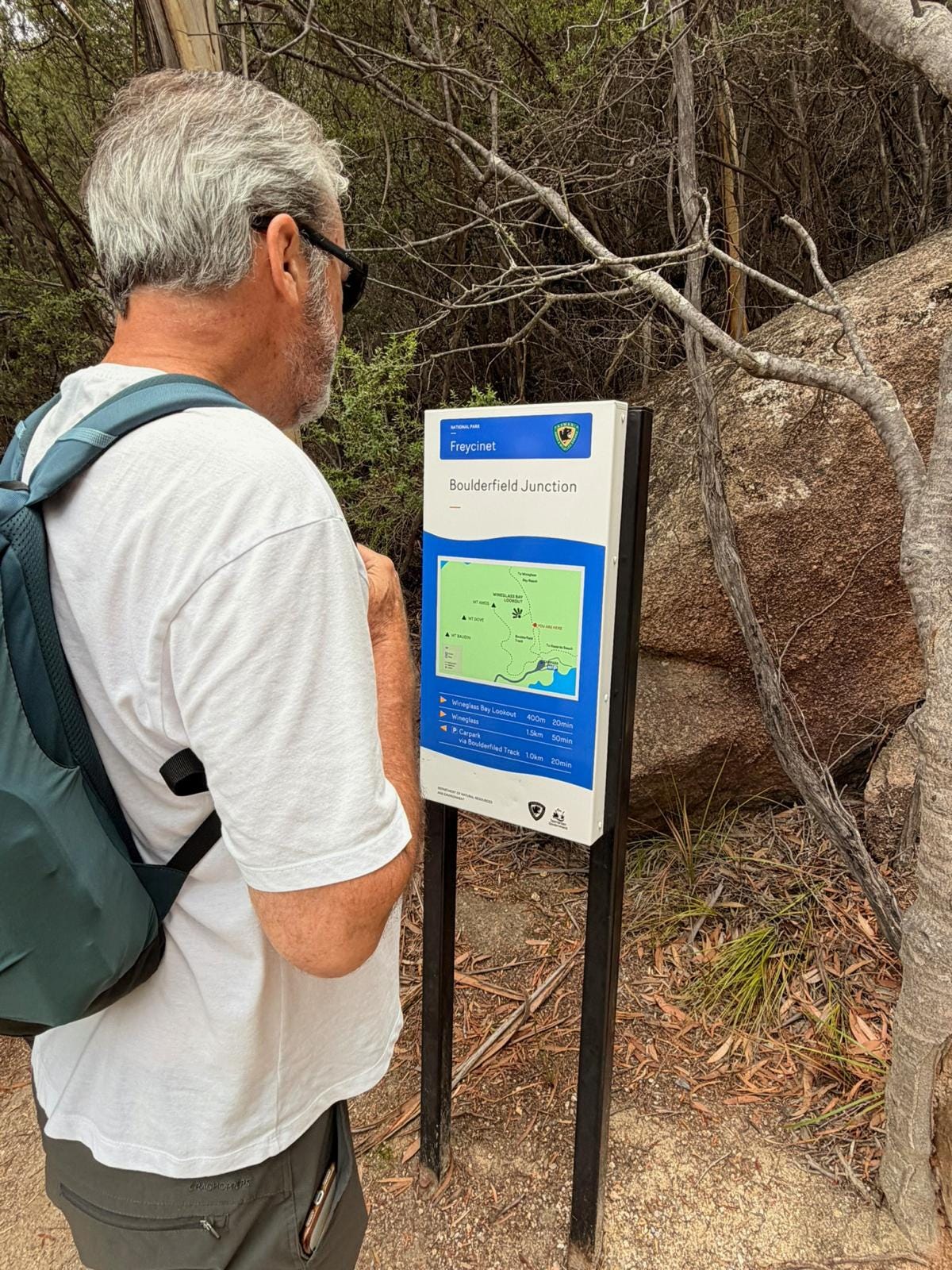 Nigel stands with a backpack reading a trail map sign at Freycinet National Park in Tasmania. Nigel stands with a backpack reading a trail map sign at Freycinet National Park in Tasmania.