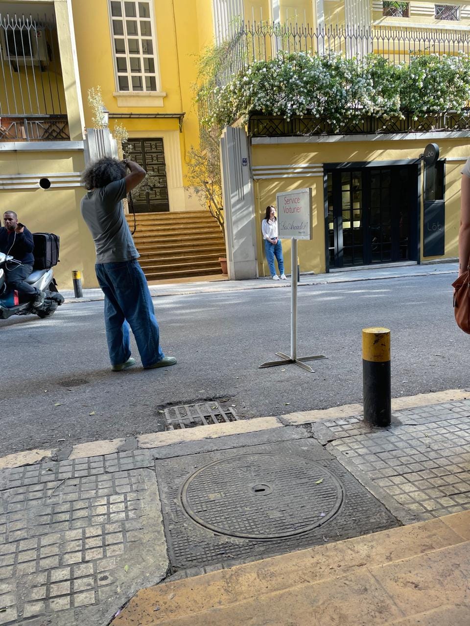 A photographer takes a photo of a subject on a street in Beirut, with a sunny yellow building in the background.
