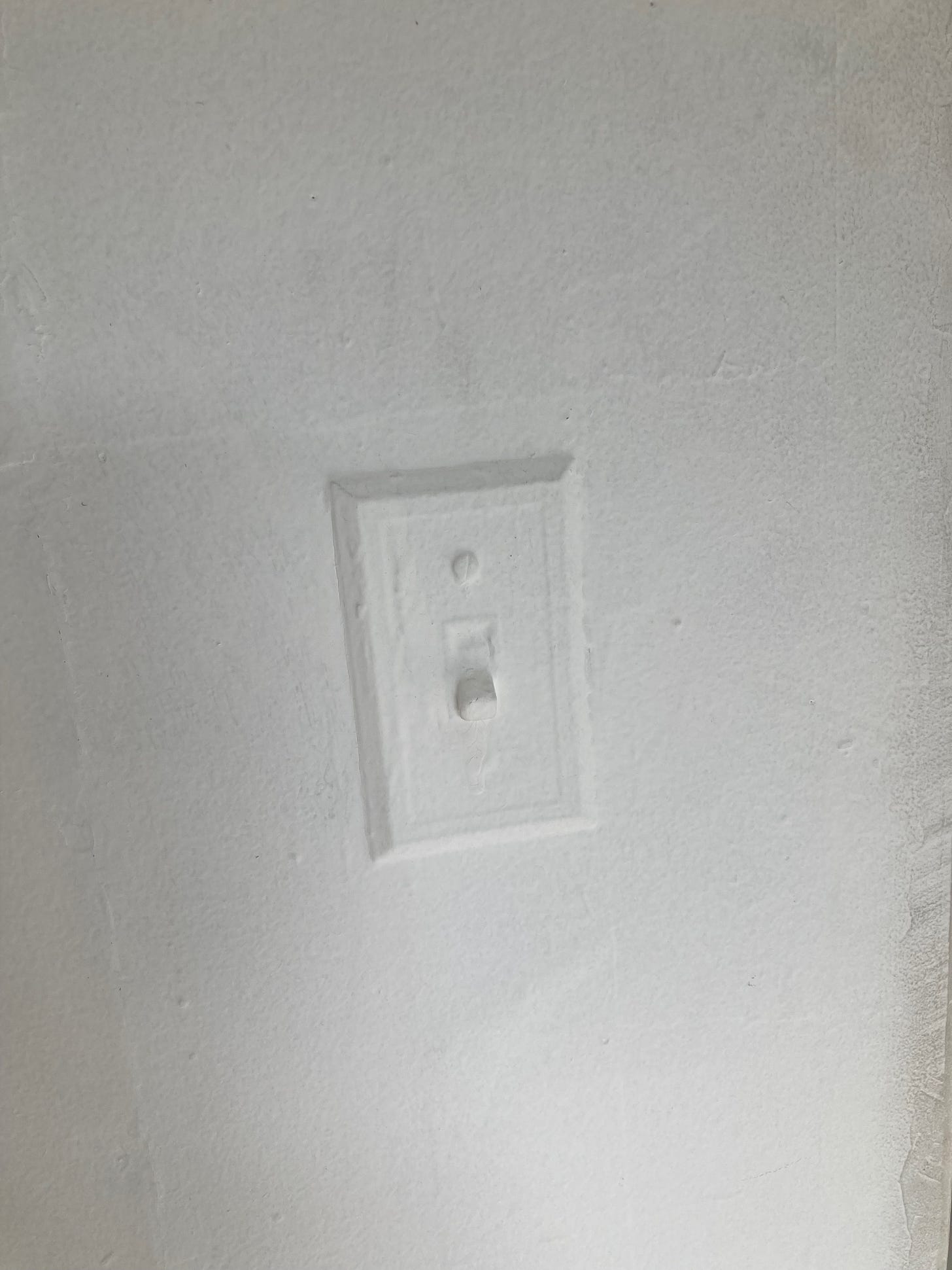 A lightswitch painted over - white walls, white paint covering all of it