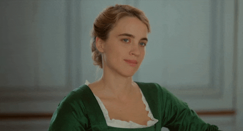gif: heloise etá de vestido vermelho. ela sorri lentamente