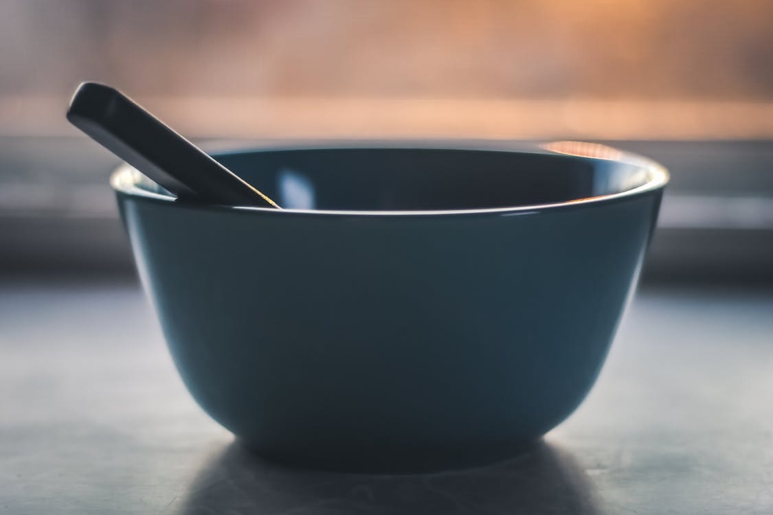 Free A minimalist photograph of an empty bowl with a spoon, set against a soft sunrise backdrop. Stock Photo