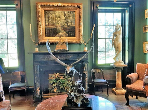 The interior of Houmas House is stately and beautiful with a wide center hall with large portraits on the wall. The second photo shows a fireplace and artwork; the third photo shows a desk in a stately room with a portrait in an ornate frame. The last photos are of bedrooms and a curving staircase.