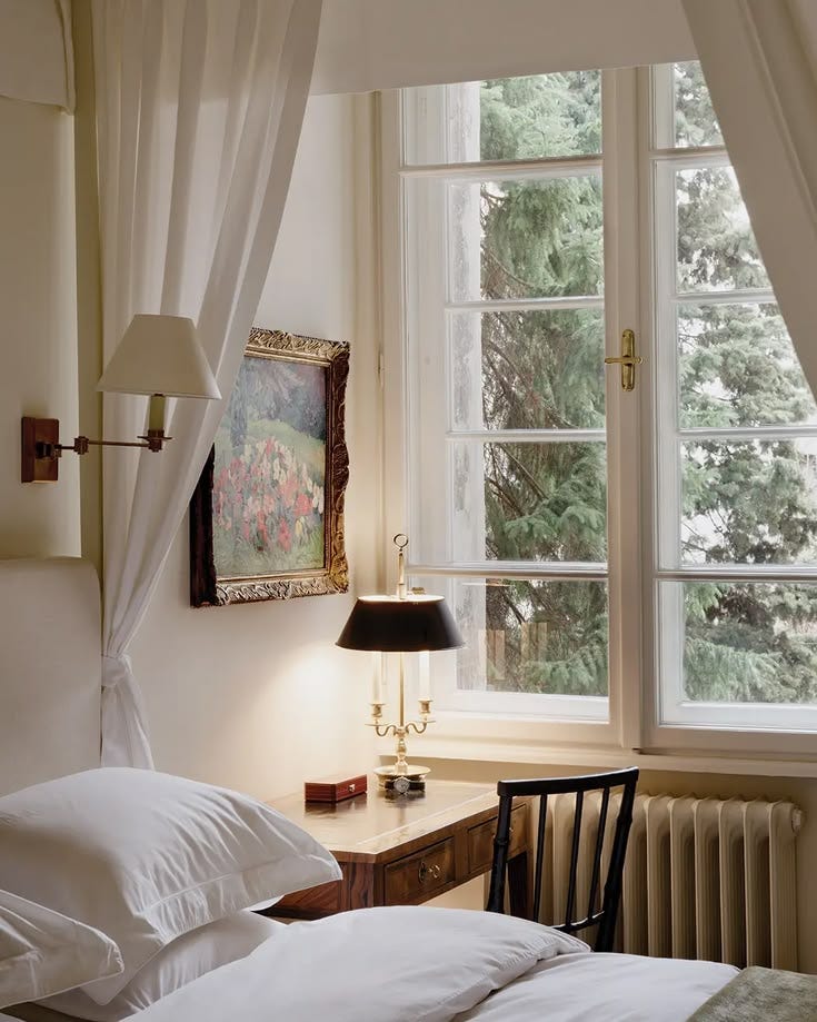 This may contain: a bed with white sheets and pillows in front of a window next to a lamp