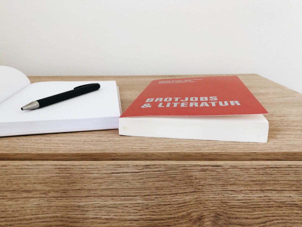 Buch Brotjob & Literatur und Notizbuch liegen auf einem Schreibtisch