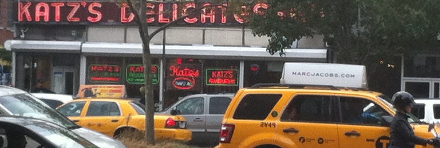 Katz's Delicatesan sign in pink neon above a row of yellow taxis
