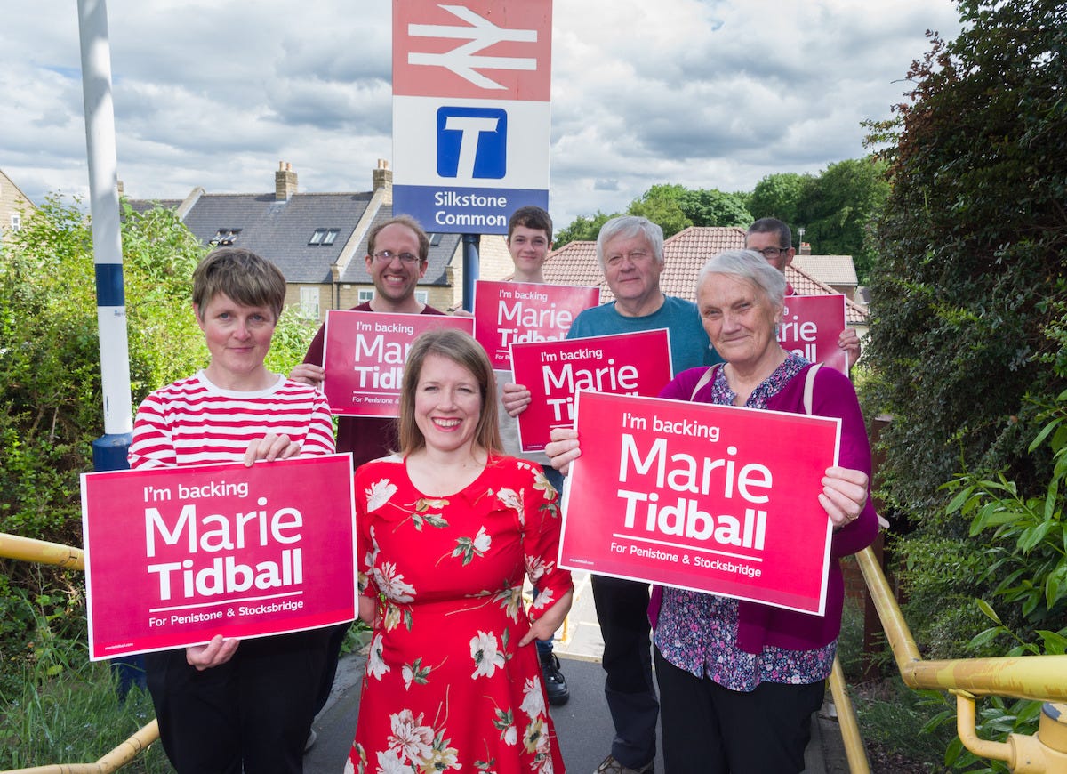 MP Marie Tidball in front of campaigners holding promotional placards