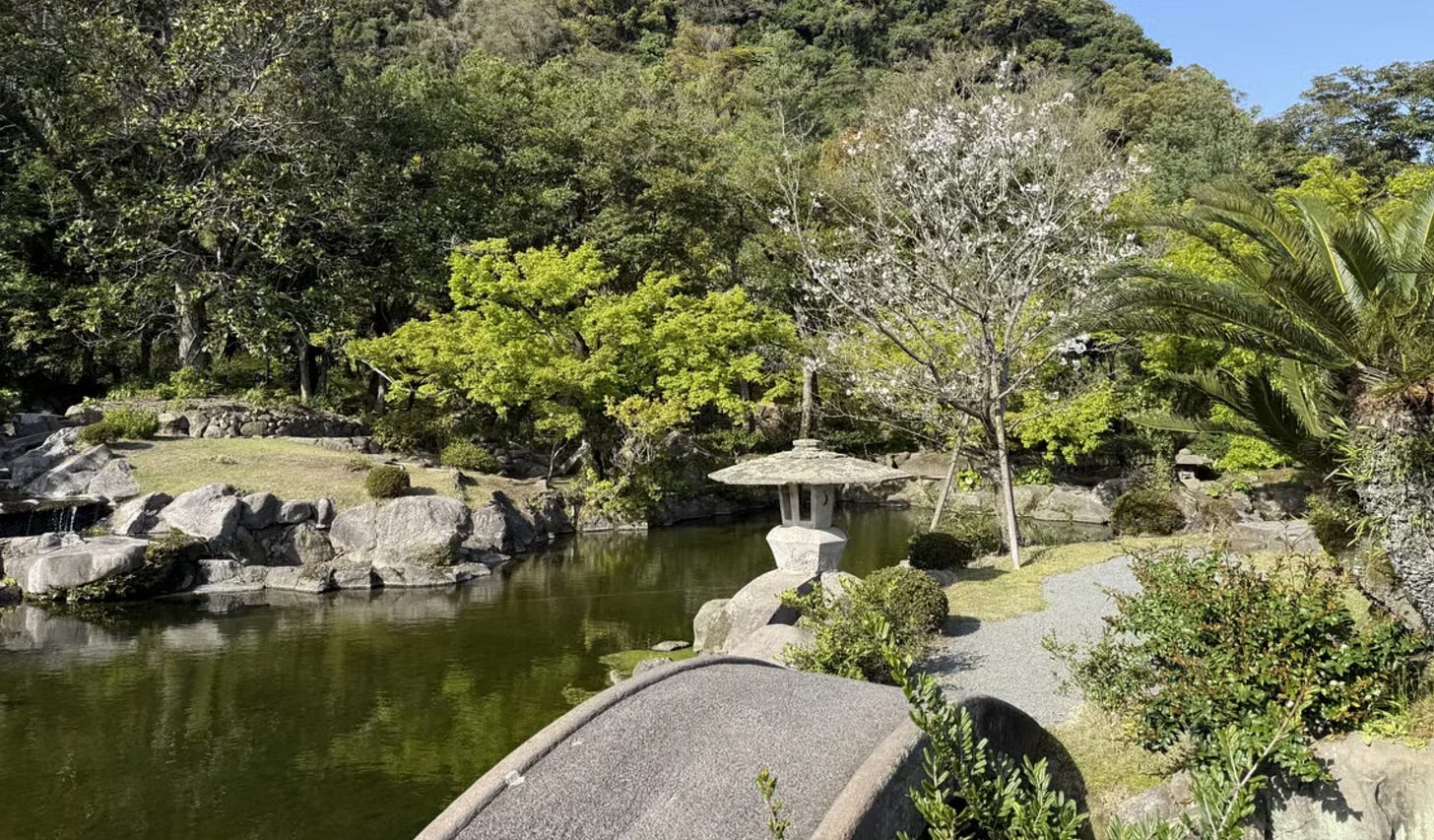 A scenic view of Sengan-en Garden featuring a stone lantern, a small bridge, and a calm pond surrounded by lush greenery.
