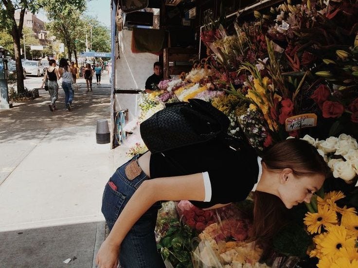 This may contain: a woman leaning against a flower stand on the sidewalk