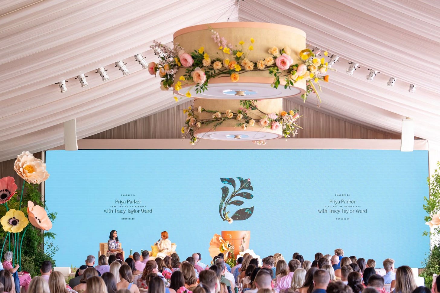 Engage! summit plenary session under a draped tent with floral chandeliers, speaker stage, and a professionally lit, well-designed audience setting.