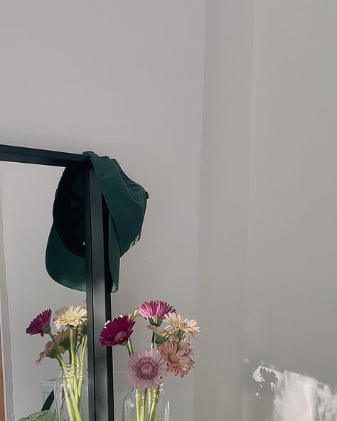 Image 1 - A cosy restaurant interior with pink and forest green decor, soft lighting, and framed artwork on the walls. / Image 2 - A hand holding a fresh cup of tea in bed, with soft pink bedding in the background. / Image 3 - Sunlight casting a warm glow on the wall, with pink flowers in a vase and a green cap resting nearby.