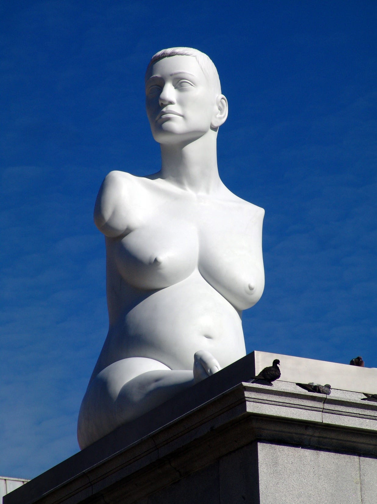A pristine white statue, like an ancient Greek marble, is viewed from below, against a bright blue London sky. Alison, who has no arms and very short legs, is sat on the plinth, heavily pregnant and naked. A pristine white statue, like an ancient Greek marble, is viewed from below, against a bright blue London sky. Alison, who has no arms and very short legs, is sat on the plinth, heavily pregnant and naked.