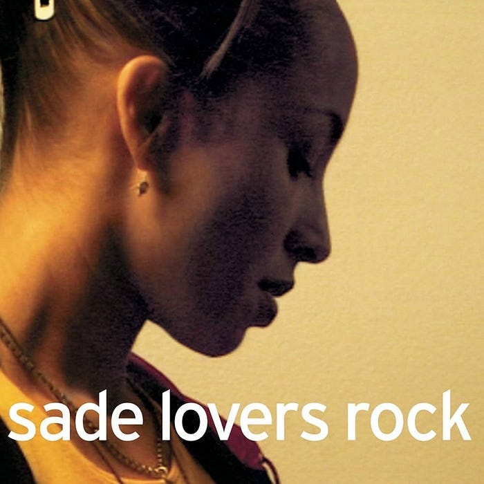 Sade is photographed from her right. She is looking downward. There is a light beige background. The album title is in white lettering across the bottom of the cover.