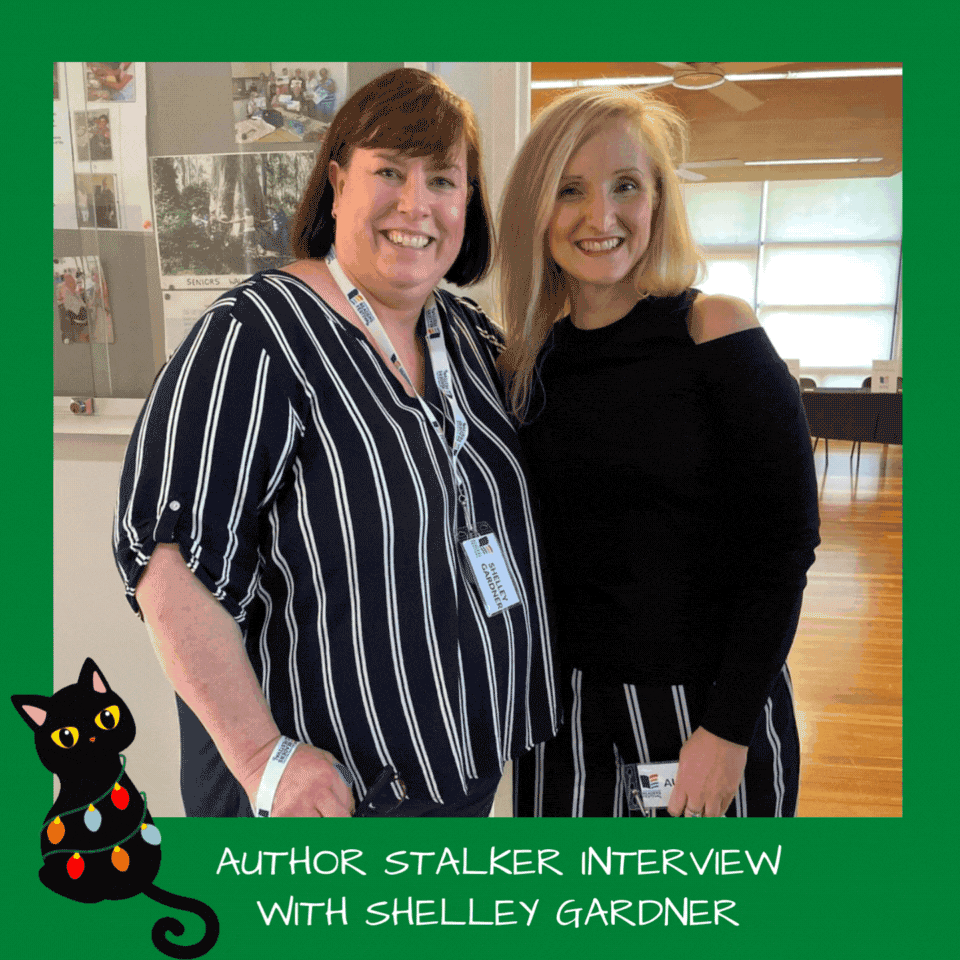 Image of two women standing next to each other with big smiles on their faces. Shelley Gardner, the woman on the left, has short brown hair, the woman on the right with long blonde hair is Belinda Alexandra. The image is surrounded by a bright green border and has a black cat cartoon wearing coloured lights.