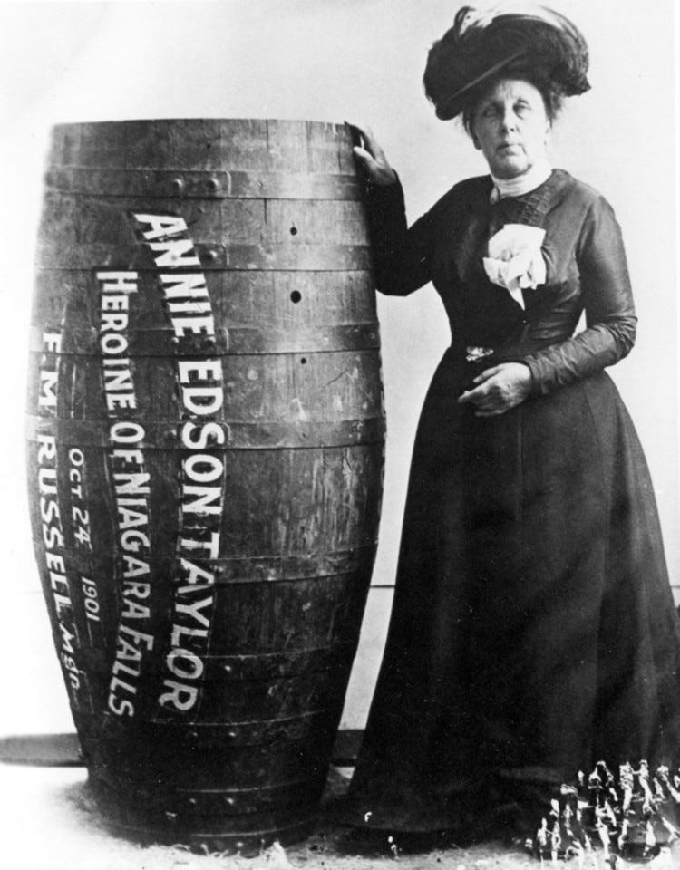 Black and white photo of Annie Edson Taylor standing next to a human-sized barrel Black and white photo of Annie Edson Taylor standing next to a human-sized barrel