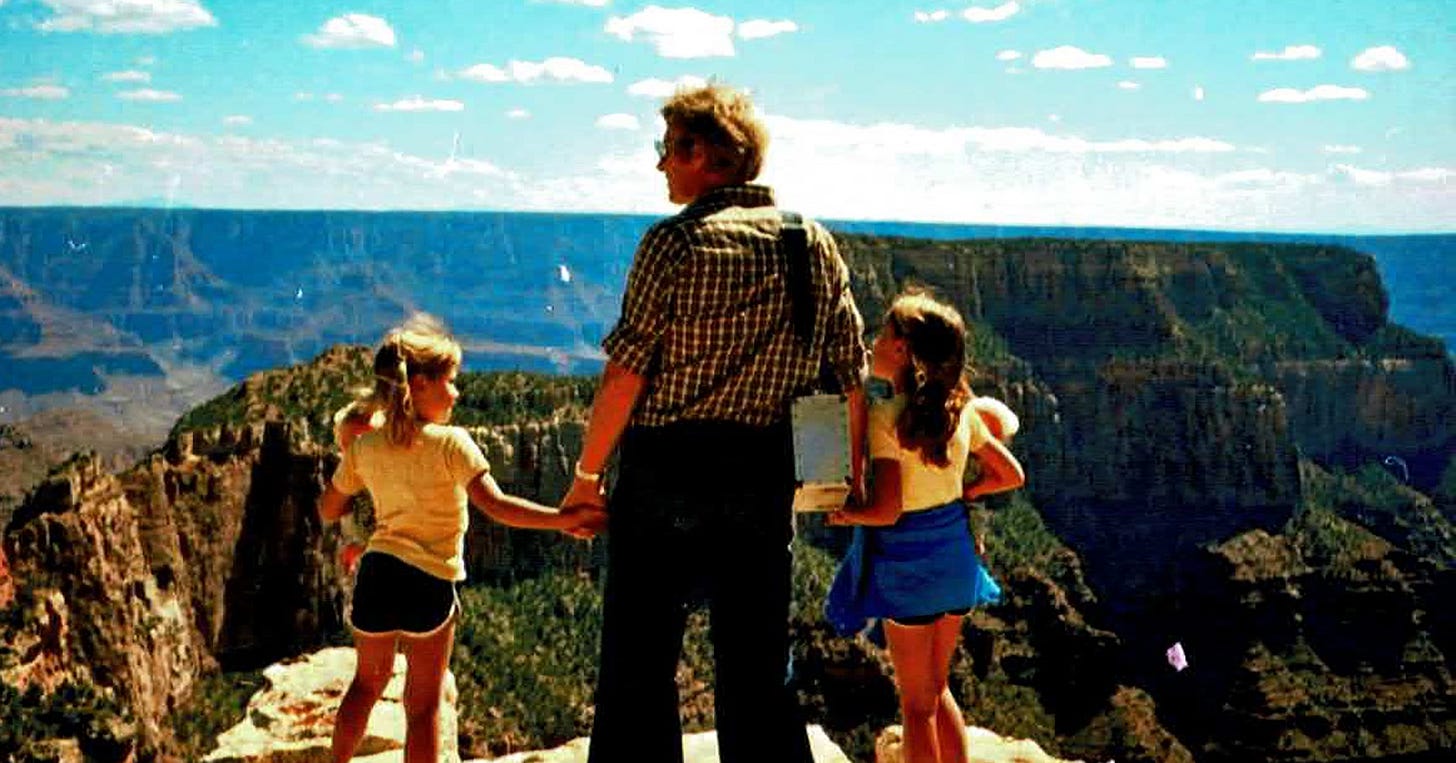 A man (Jo's dad) stands on a cliff at the Grand Canyon, holding hands with two children (Jo and her sister), admiring the breathtaking landscape under a blue sky.
