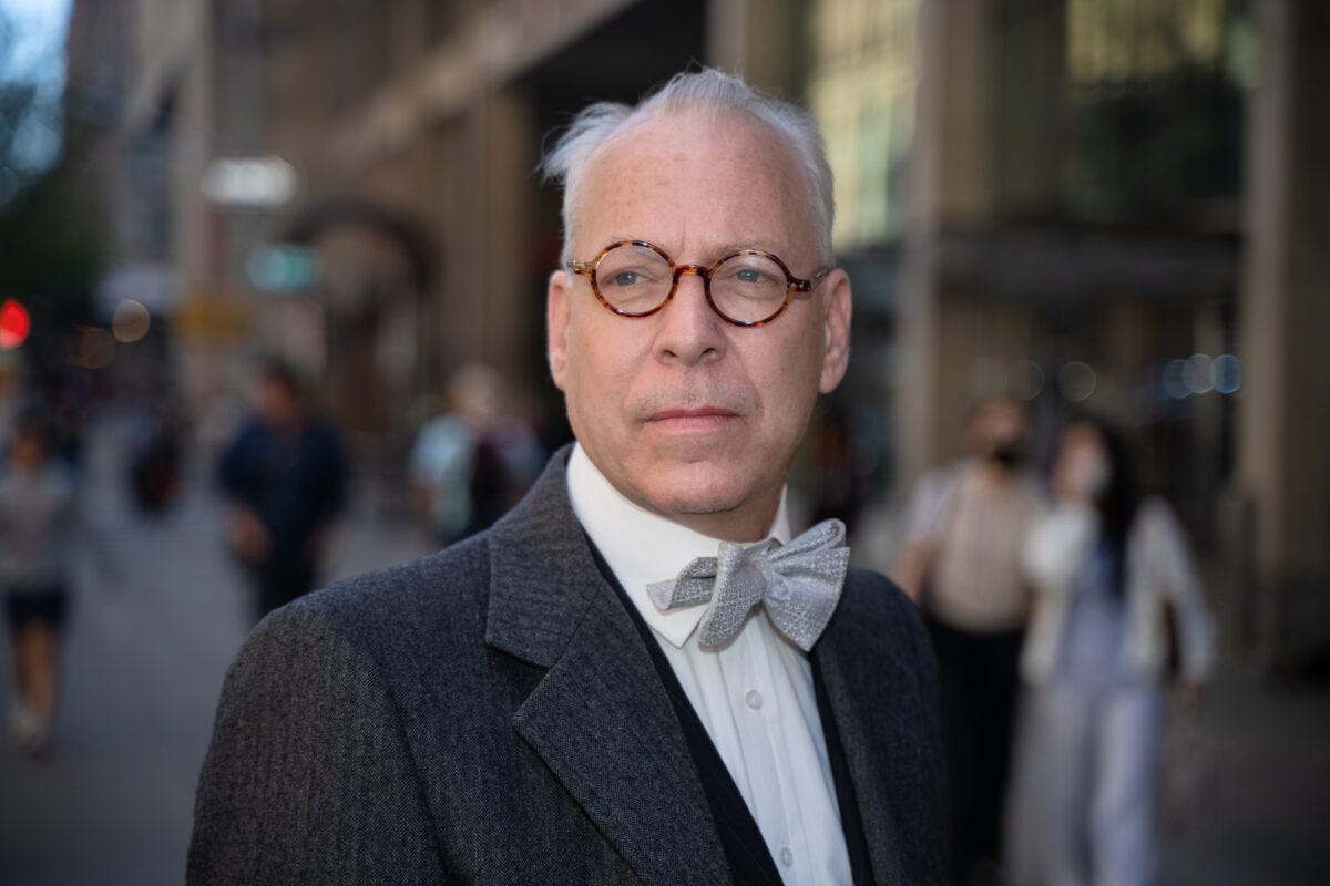Jeffrey Tucker in round tortoiseshell glasses and a silver bow tie stands on a busy city street. Jeffrey Tucker in round tortoiseshell glasses and a silver bow tie stands on a busy city street.