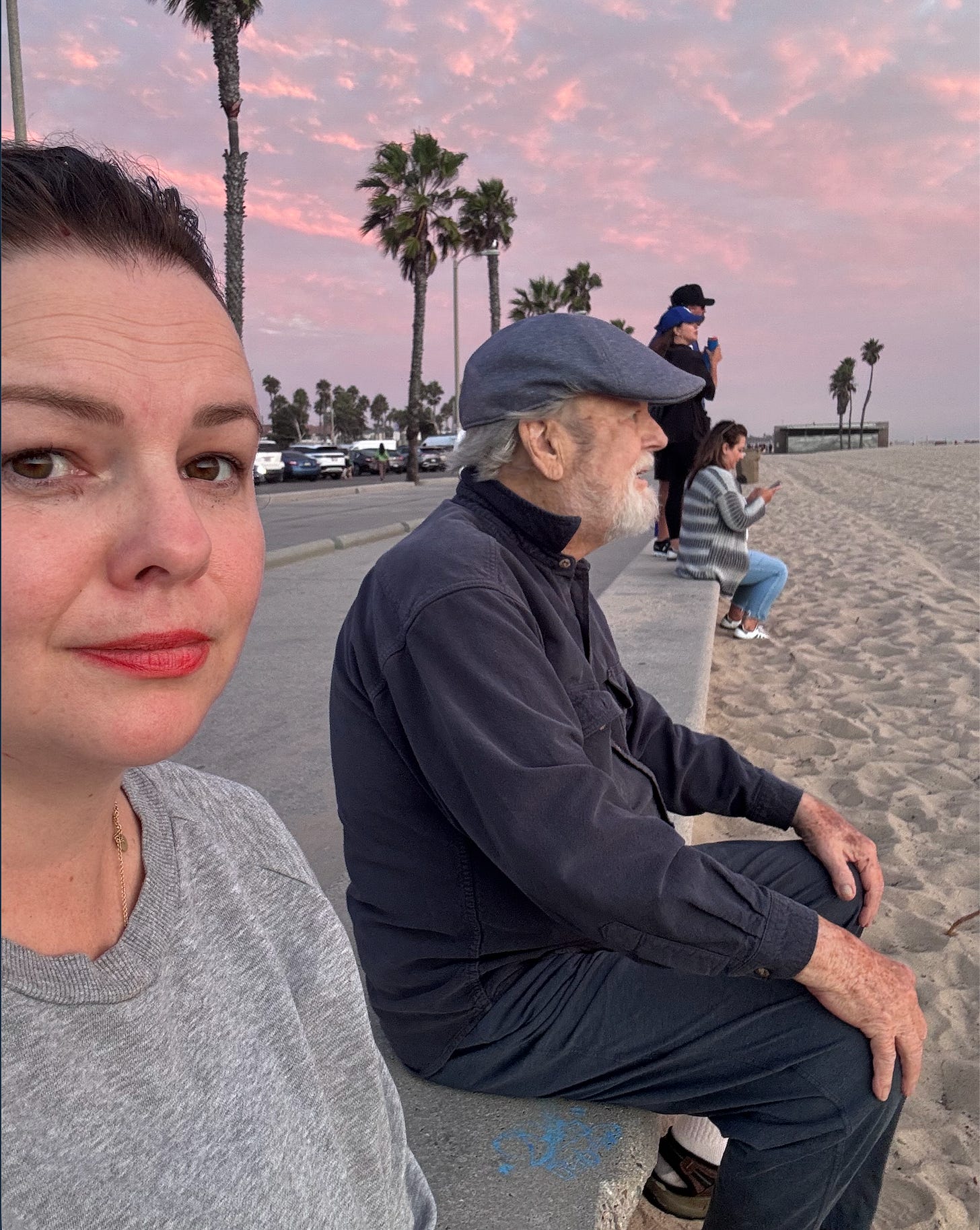 Amber and her dad sit by the beach during sunset. Amber has her head turned so that she is looking into the camera and smiling slightly while her dad looks straight ahead at the ocean.