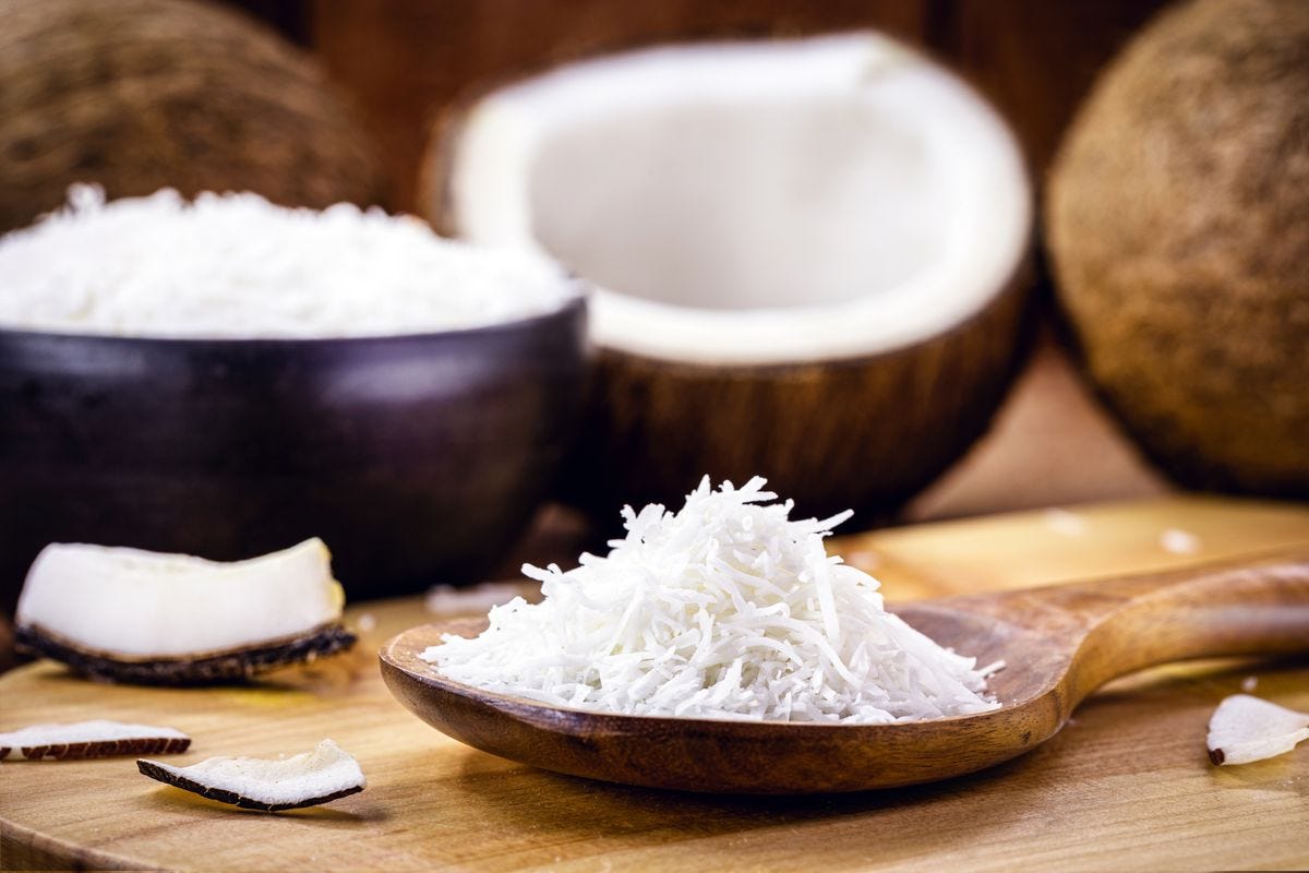 Whole coconuts and shredded coconut meat siting in a large wooden spoon Whole coconuts and shredded coconut meat siting in a large wooden spoon